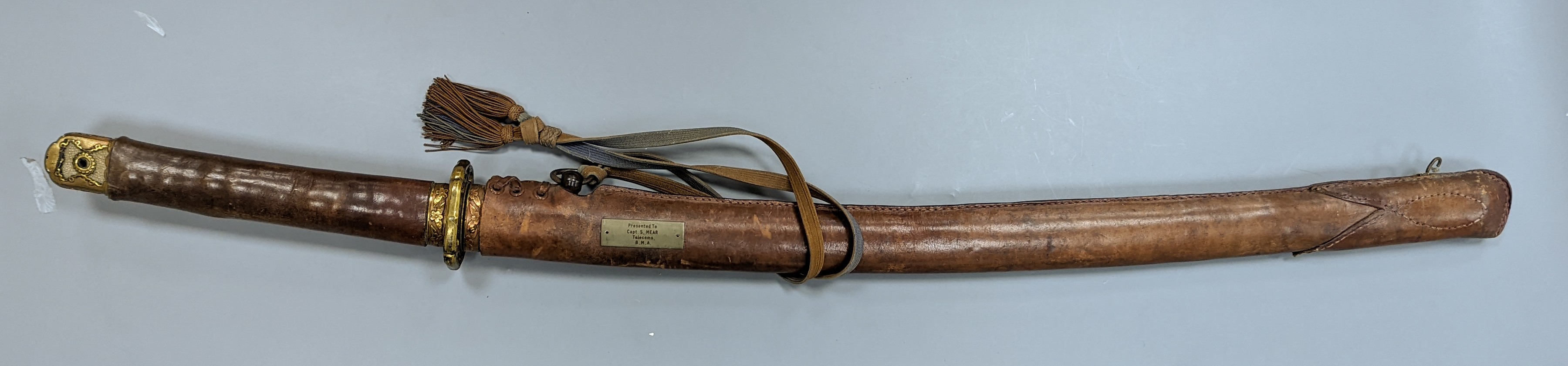 A Japanese Katana with leather covered sheath, plaque reading ‘Presented to Capt. S. Mear Telecoms B.M.A’ 93 cms long.